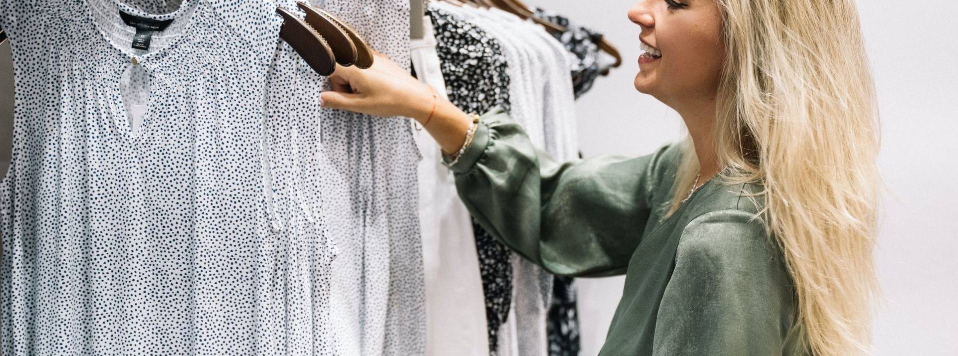 Devant l’urgence de rendre la mode + responsable, Camaieu décide de mesurant l’impact de ses collections et d’afficher en toute transparence pour ses clientes l’éco-note de ses produits. Femme devant un portant de chemisier dans une boutique