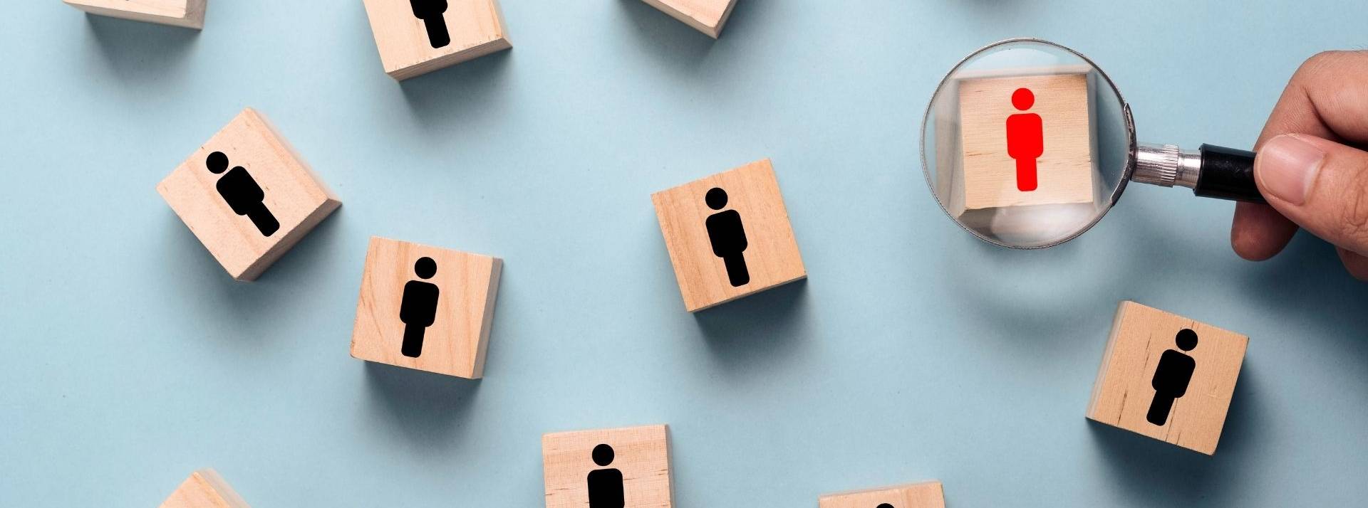 LinkedIn dévoile son classement des 25 métiers pour lesquels la demande a le plus progressé en France ces dernières années. Main tenant le verre de loupe à la recherche d’icône humaine rouge sur le bloc de cube en bois parmi l’icône de personnes noires. Concept de développement humain