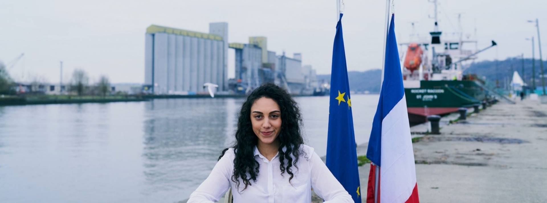Le collectif du Pacte du Pouvoir de Vivre, à l’initiative de cette démarche avec son agence Josiane, a publié « Les Vœux des Français » Jeune femme assise derrière un bureau avec les drapeaux français et européen
