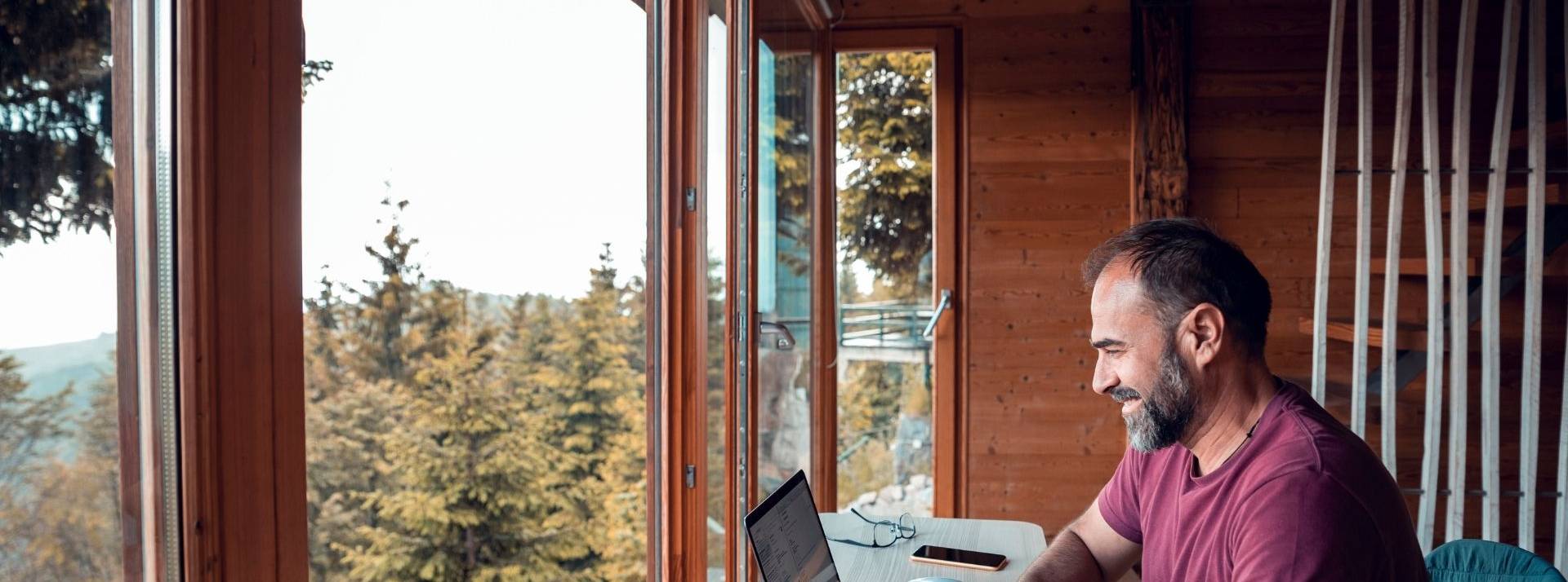 PrestaShop réinvente le Work from Anywhere et annonce le recrutement de 200 talents en 2022 Homme travaillant devant une baie vitrée qui donne sur la nature