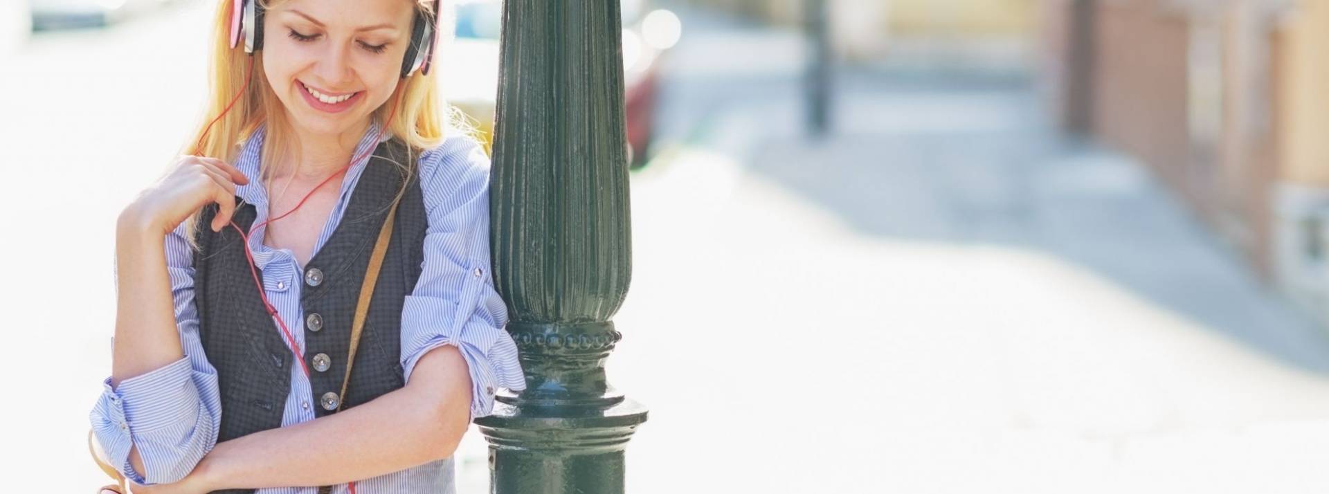 Rewind lève 700k€ en Seed auprès de Kima Ventures pour démocratiser son offre de Self-Guided Tours en France et en Europe. Jeune femme adossé à un lampadaire avec un casque sur les oreilles et un appareil photo autour du cou