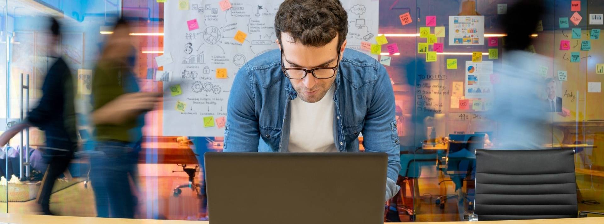 Le réseau d'innovation national 1Kubator annonce l’acquisition de la première plateforme régionale de financement participatif en capital, Incit’financement. Homme travaillant dans un bureau créatif à l’aide de son ordinateur et personnes se déplaçant en arrière-plan