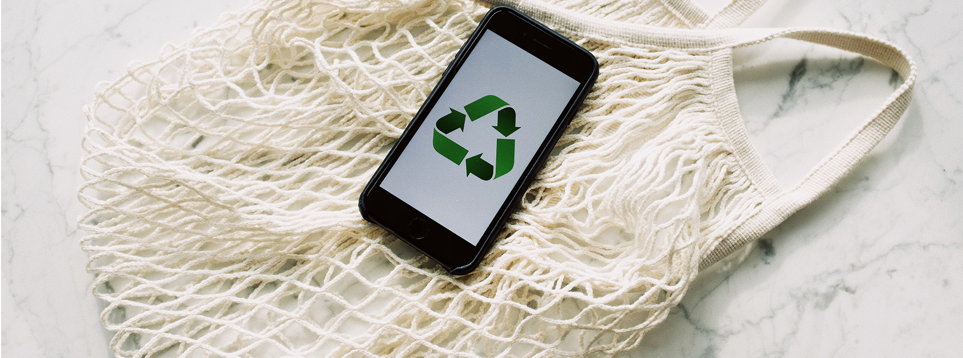 Une startup utilisant l'open banking pour créer un programme de fidélité pour la planète Sac de course avec un portable sur lequel se trouve le logo du recyclage