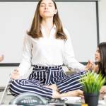 Femme assise en position du lotus au milieu d'un bureau avec des collègues stressées autours