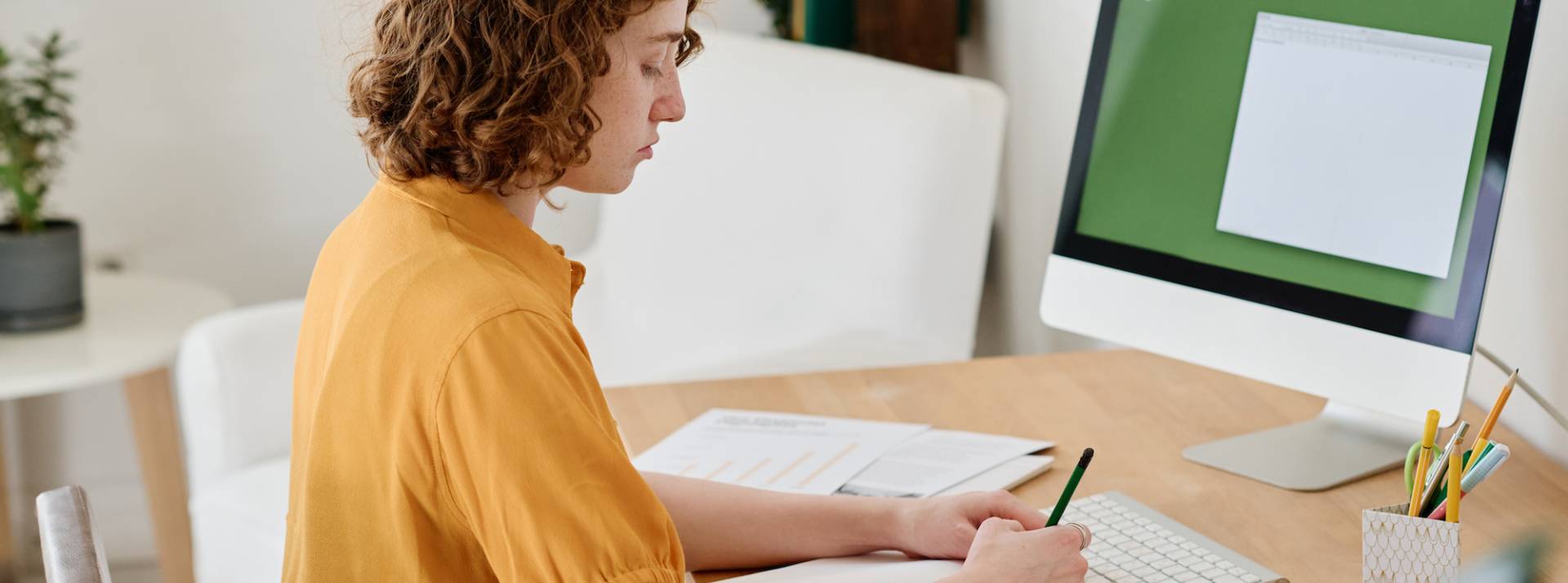 Side view of young businesswoman in casualwear working in front of computer Side view of young businesswoman in casualwear working in front of computer