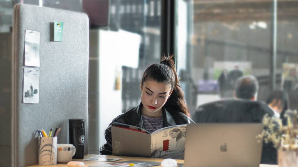 Papier ou numérique : le vrai du faux sur leur impact écologique femme qui lit un ouvrage avec un ordinateur sur son bureau
