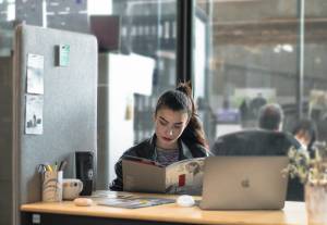 femme qui lit un ouvrage avec un ordinateur sur son bureau