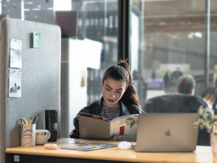 femme qui lit un ouvrage avec un ordinateur sur son bureau